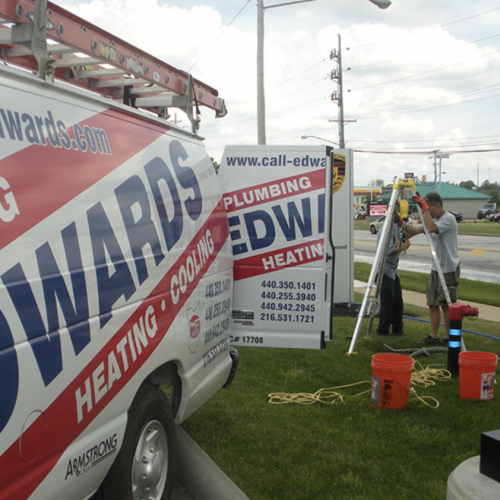 A picture of an Edwards Plumbing Heating and Cooling truck with employees working in the background