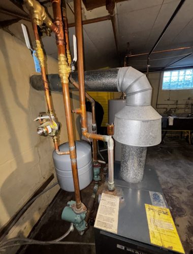 Boiler system with copper piping, expansion tank, and circulator pump installed in basement.