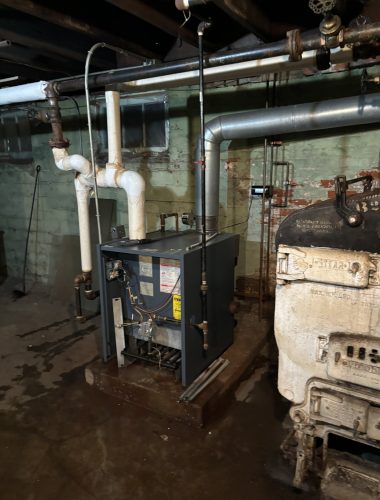 Gas boiler installed next to older cast iron steam boiler during replacement project.