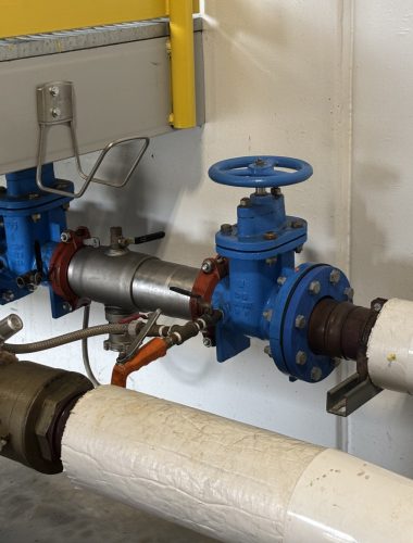 Edwards technician's commercial double-check backflow preventer installation with blue gate valves on an insulated water line in a Northeast Ohio mechanical room